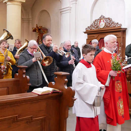 Der Pfarrer geht singend durch den Mittelgang der Kirche. Neben und hinter ihm sind Menschen mit Palmzweigen in den Händen.