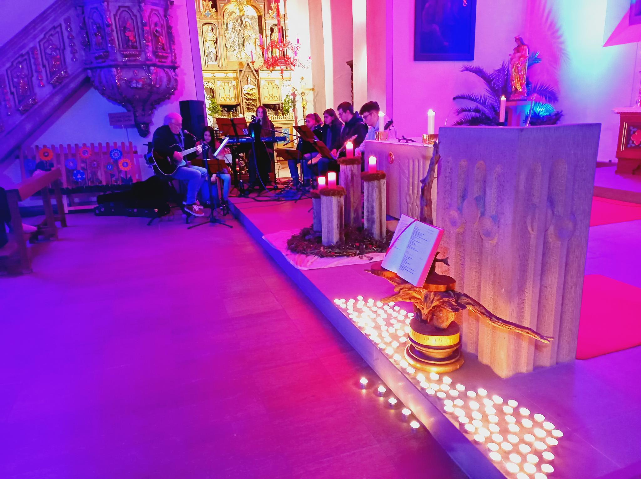 etwa 100 Teelichter stehen vor dem Ambo auf dem Boden, im Hintergrund sieht man die Band und den brennenden Adventskranz