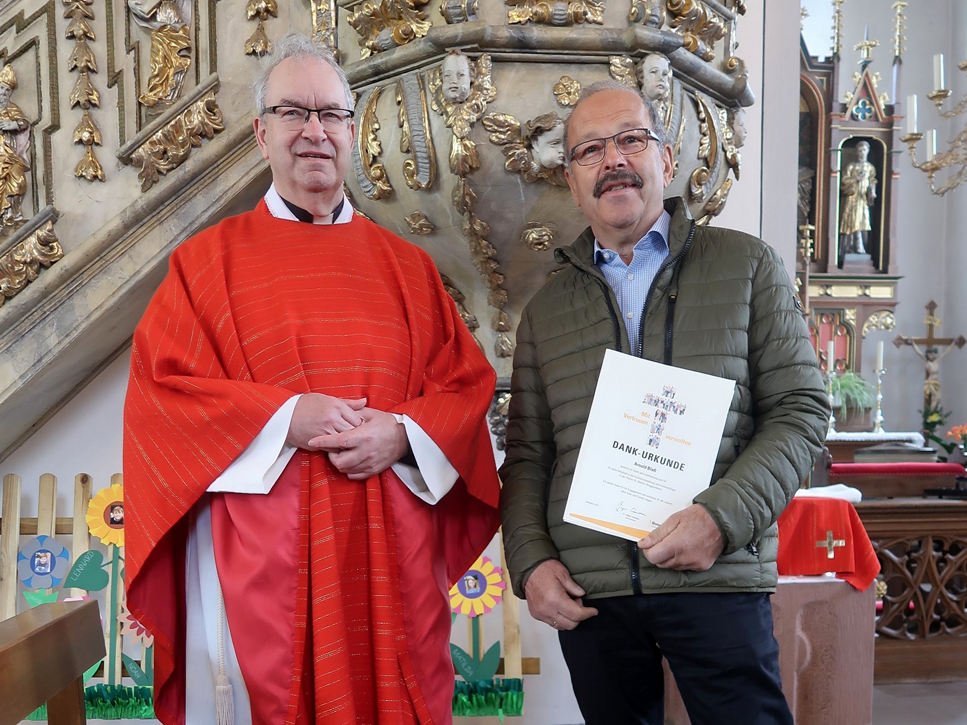 Der Pfarrer und Herr Blass stehen nebeneinander und schauen in die Kamera.