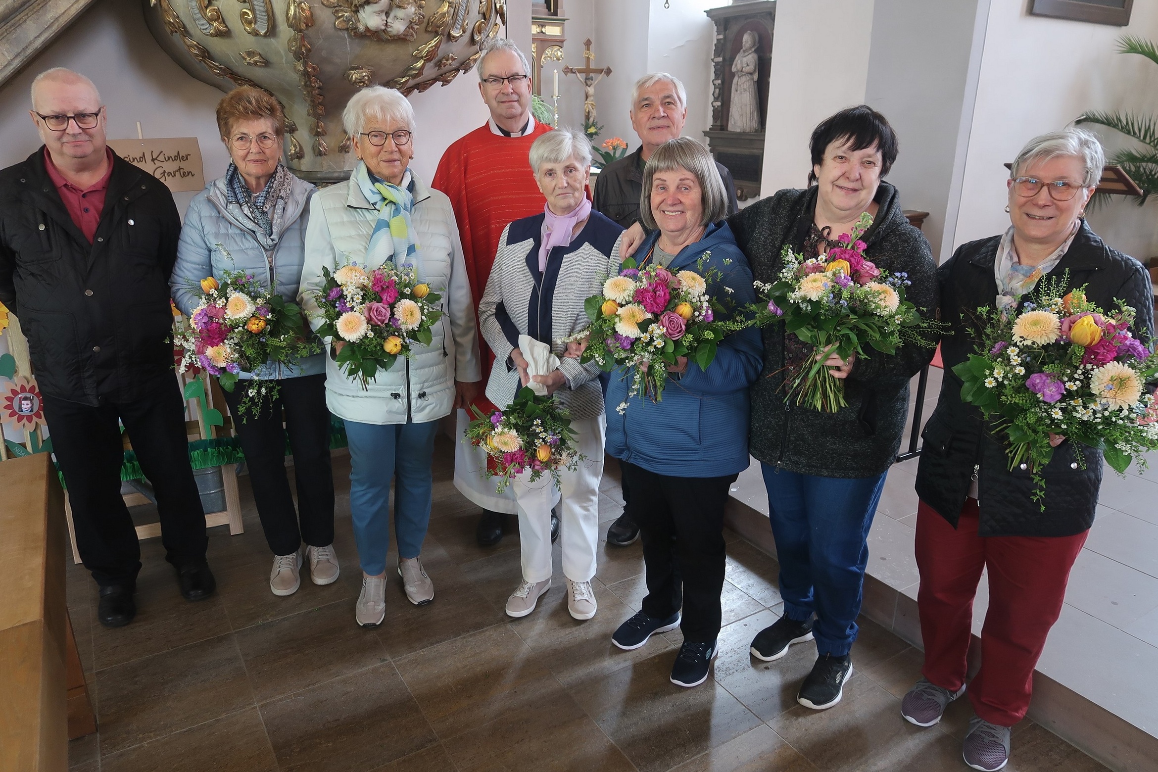 Auf dem Foto stehen neun Frauen und Männer zusammen. Die Frauen halten Blumensträuße in den Händen.