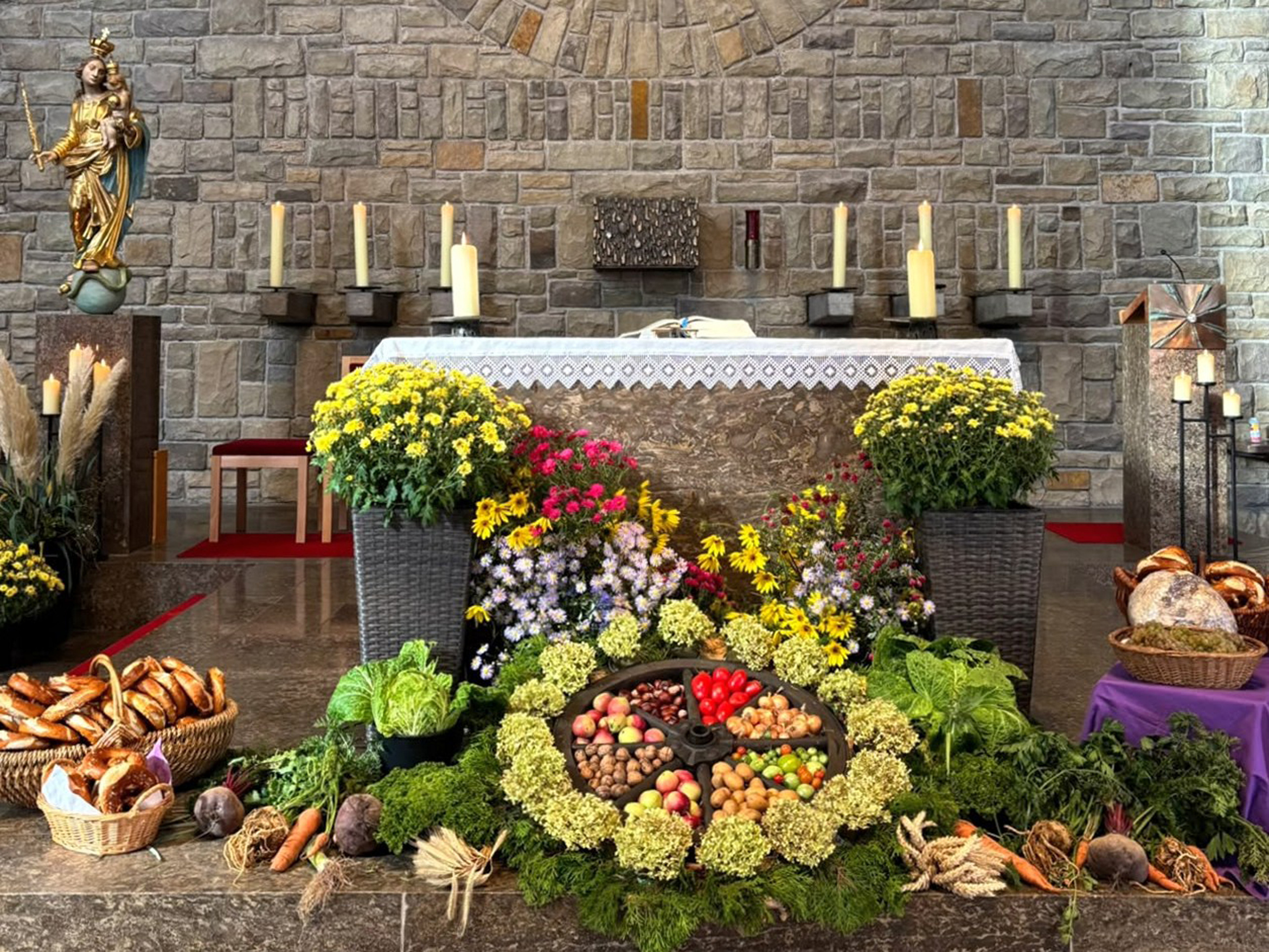 Das Bild zeigt einen Altar in einer Kirche. Neben und vor dem Altar sind Blumen, Gemüse und Obst dekoriert. 