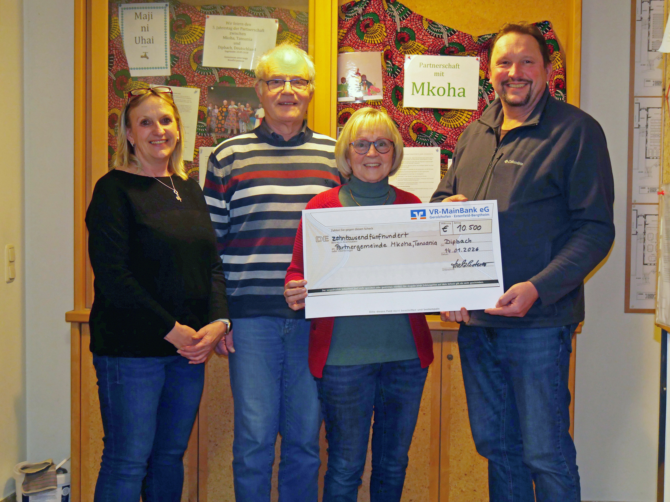 Ein Gruppenbild mit vier Personen. Zwei von ihnen halten den großen Spendenscheck.
