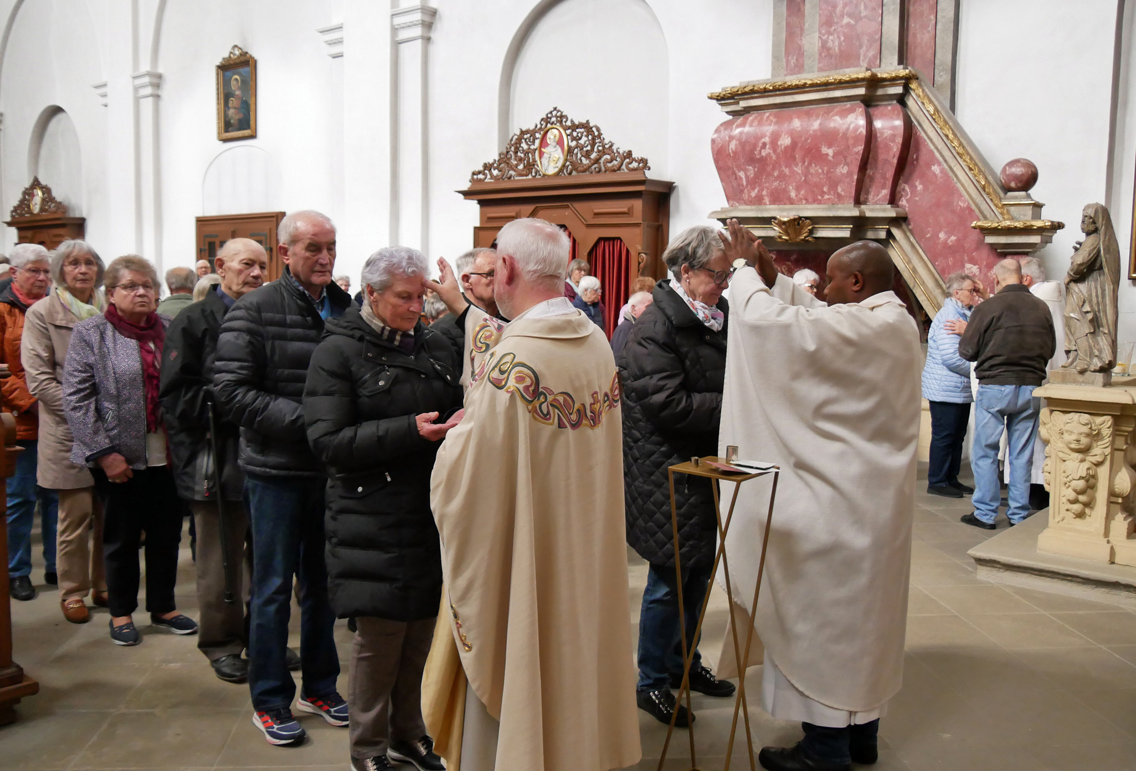 Zwei Prister legen Menschen die Hand auf die Stirn. Die Priester sind von hinten, die Menschen von vorne.