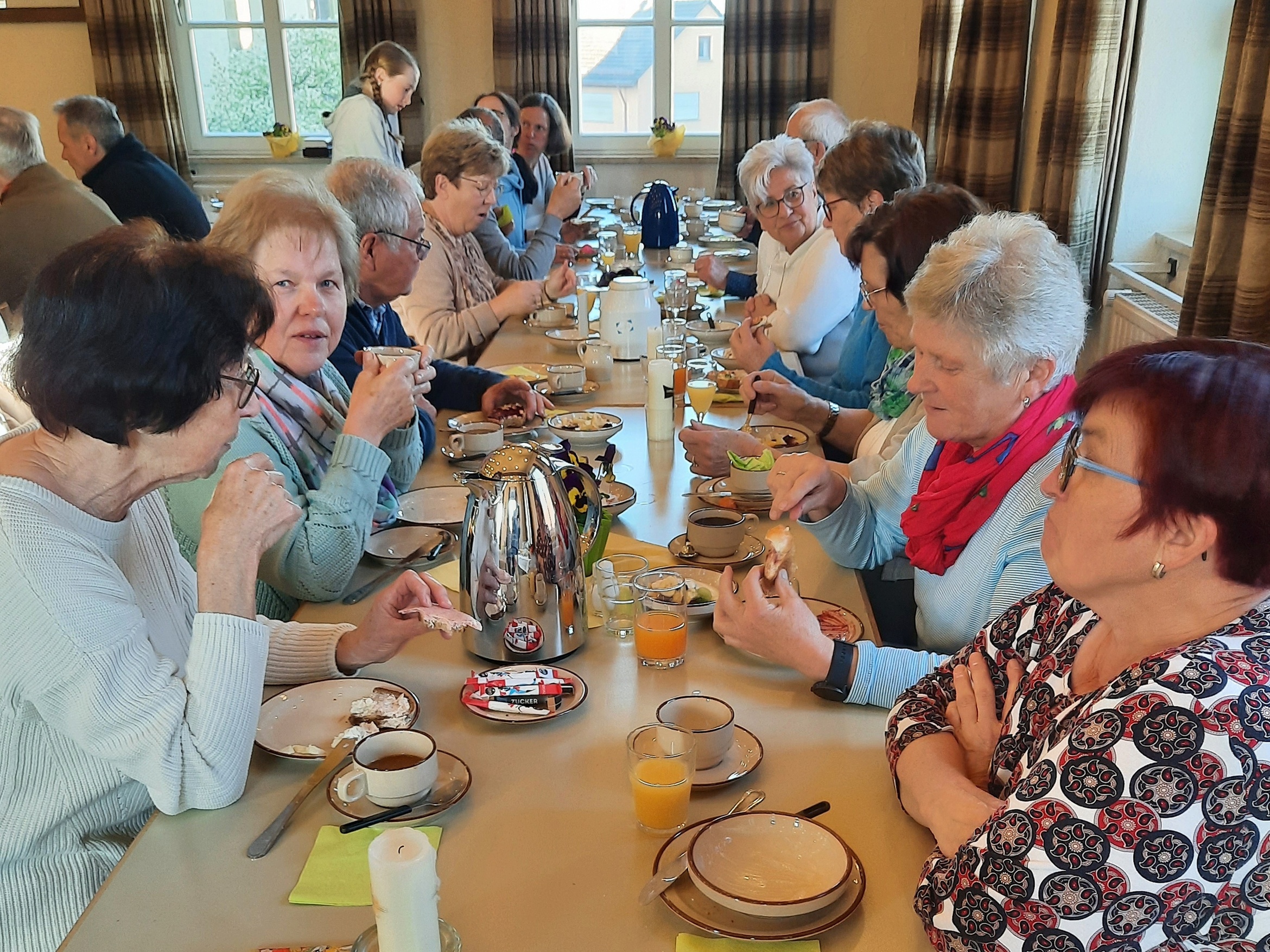 An einem Tisch sitzen rechts und links mehrere Personen und frühstücken.