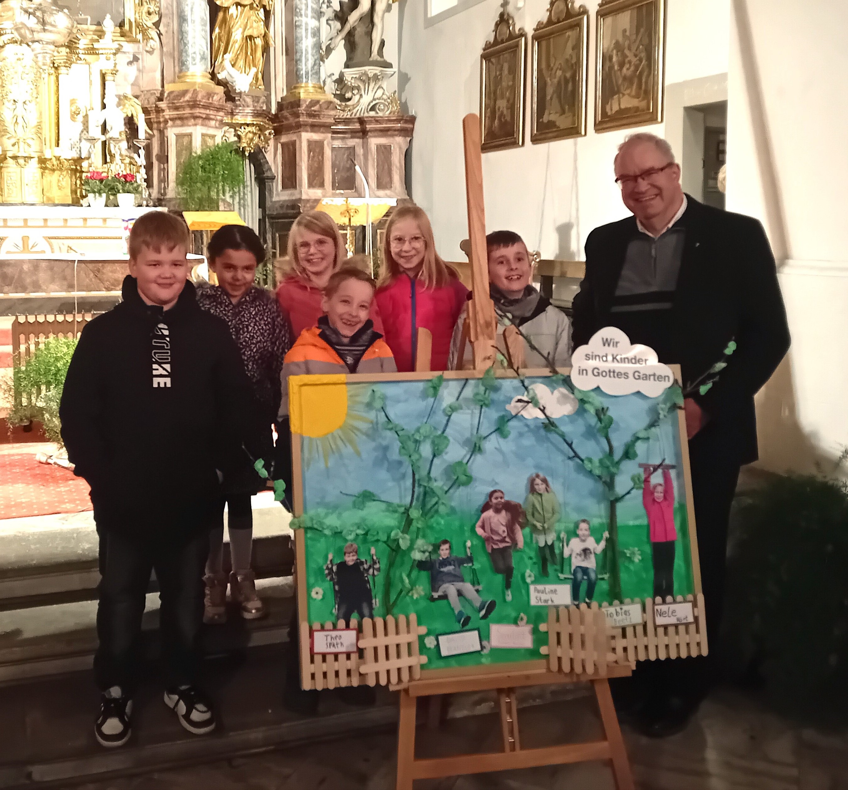 Die Kommunionkinder stehen zusammen mit dem Pfarrer hinter einem großen Bild, welches einen Garten zeigt und welches die persönlichen Vorstellungen der Kinder enthält.