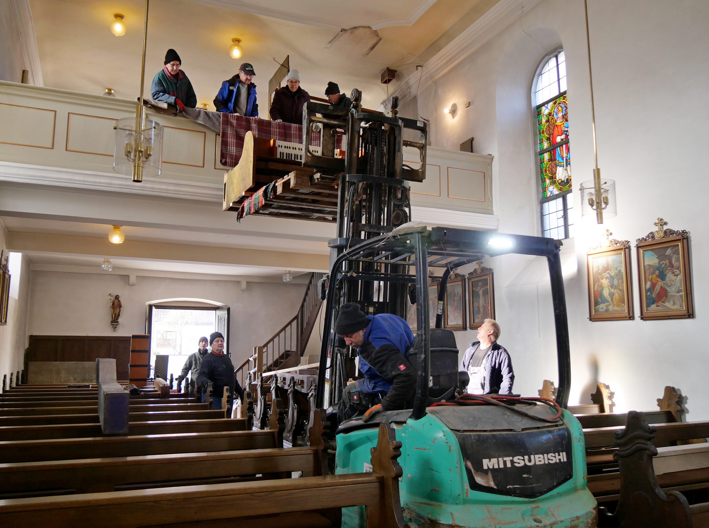 Ein Gabelstapler steht in der Kirche. Die Orgel wird gerade auf die ausgefahrene Gabel gelegt.