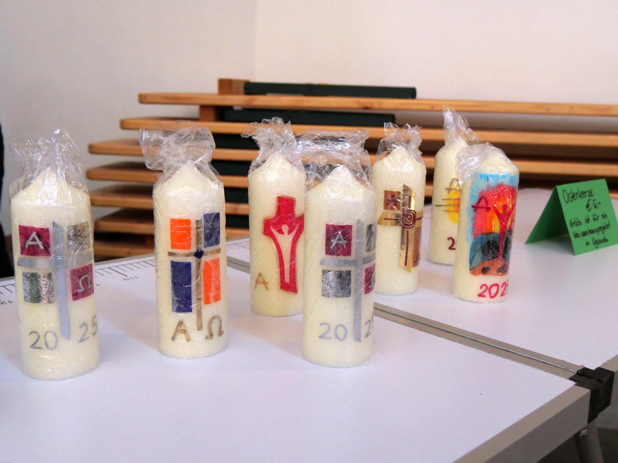 Auf einem Tisch stehen sieben Osterkerzen mit unterschiedlichen Motiven.