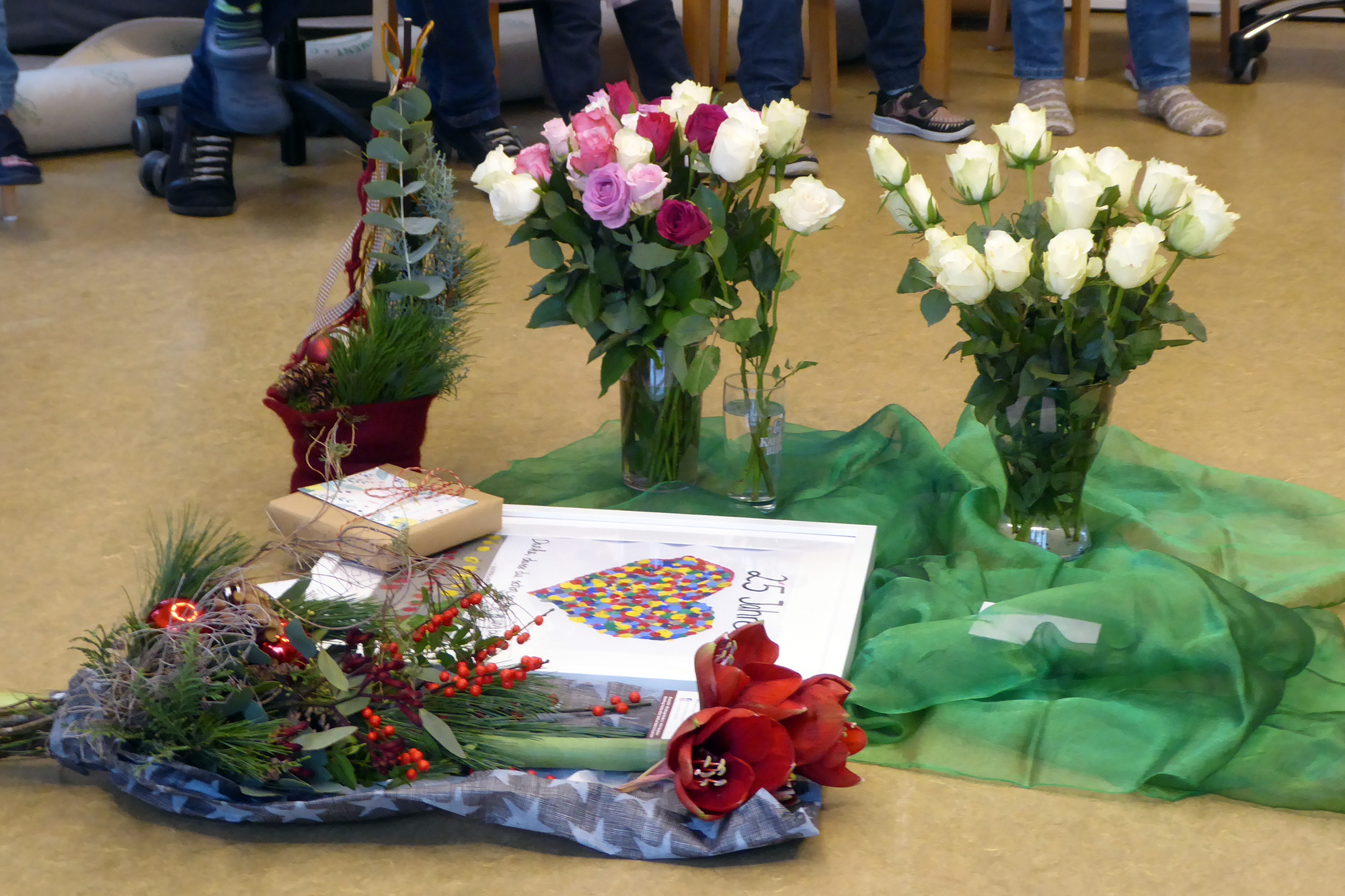 Auf einem grünen Tuch auf dem Boden stehen Blumen und Geschenke.