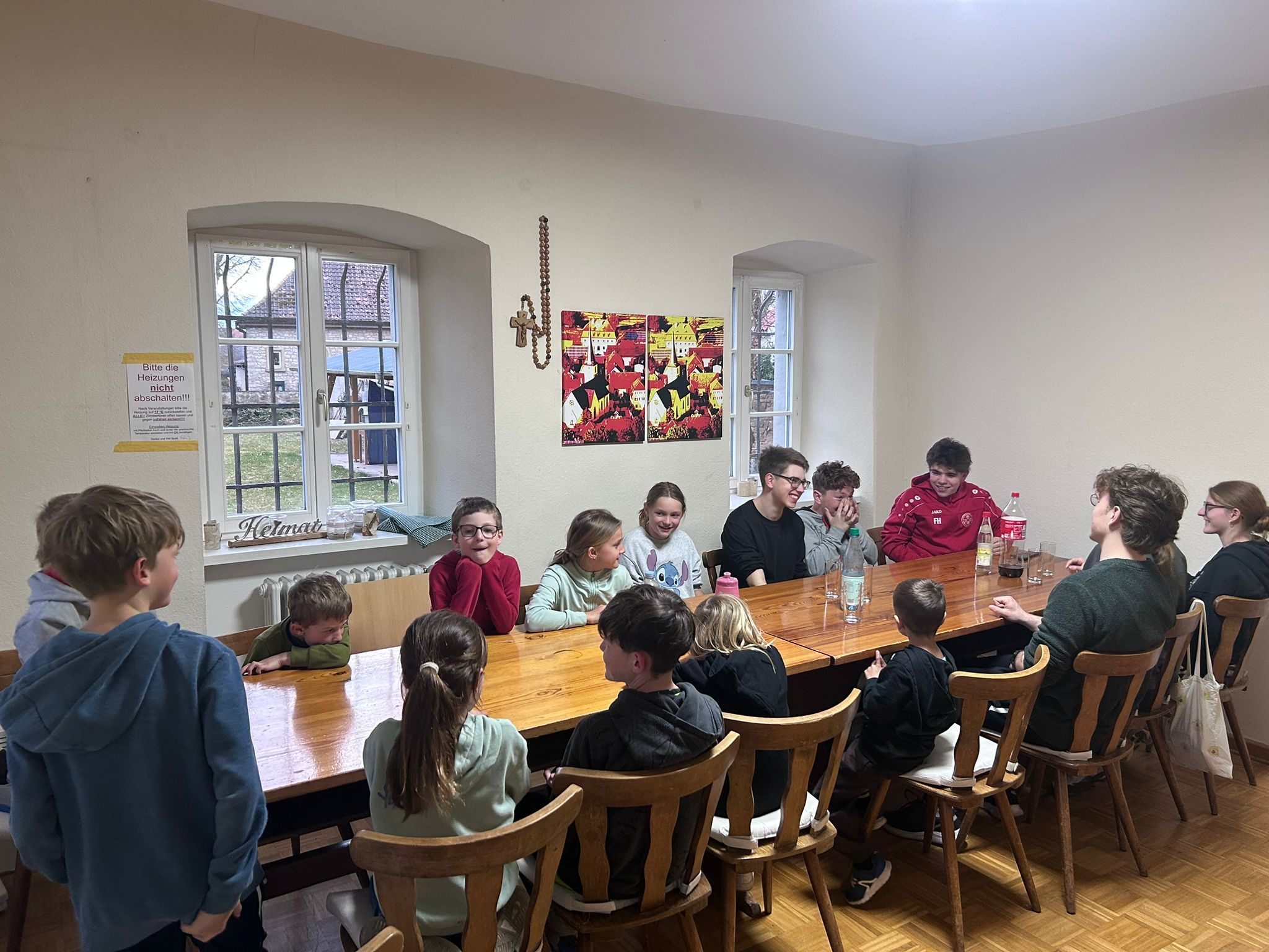 Etwa 15 Kinder und Jugendliche sitzen sich an einem langen Tisch gegenüber, auf  dem Tisch stehen einzelne Getränke.