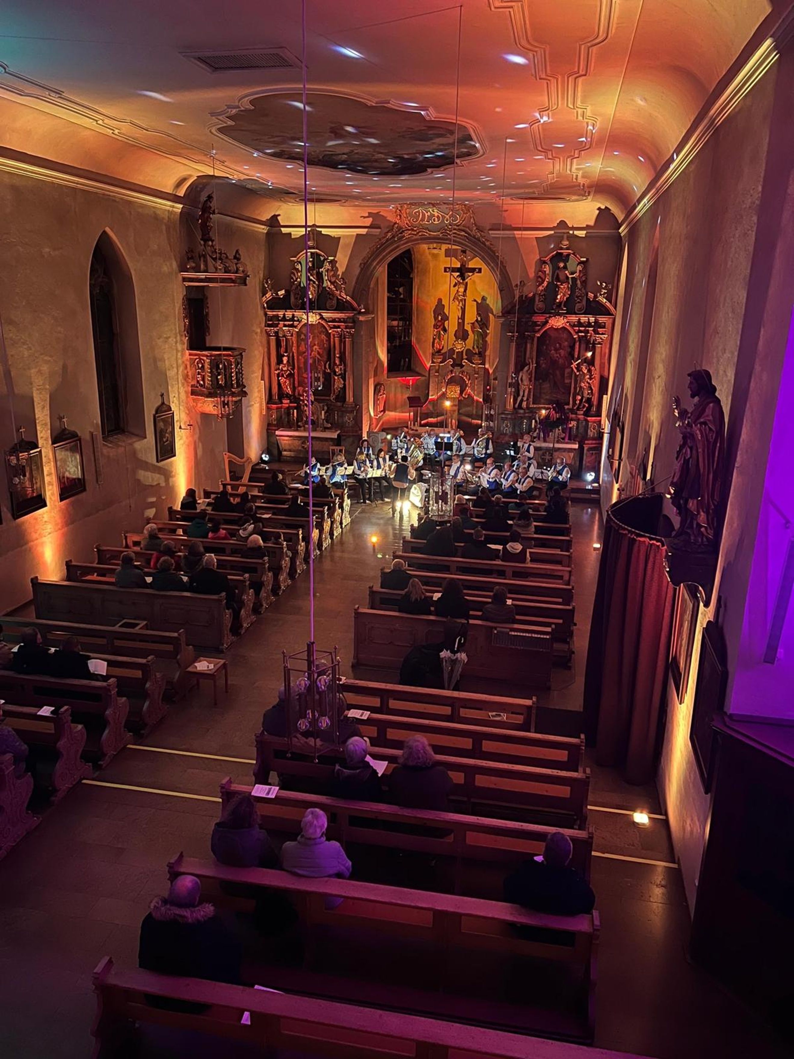 Blick von der Empore in die Kirche; Die Kirche ist bunt ausgeleuchtet, vor dem Altarraum sitzen die Musiker.