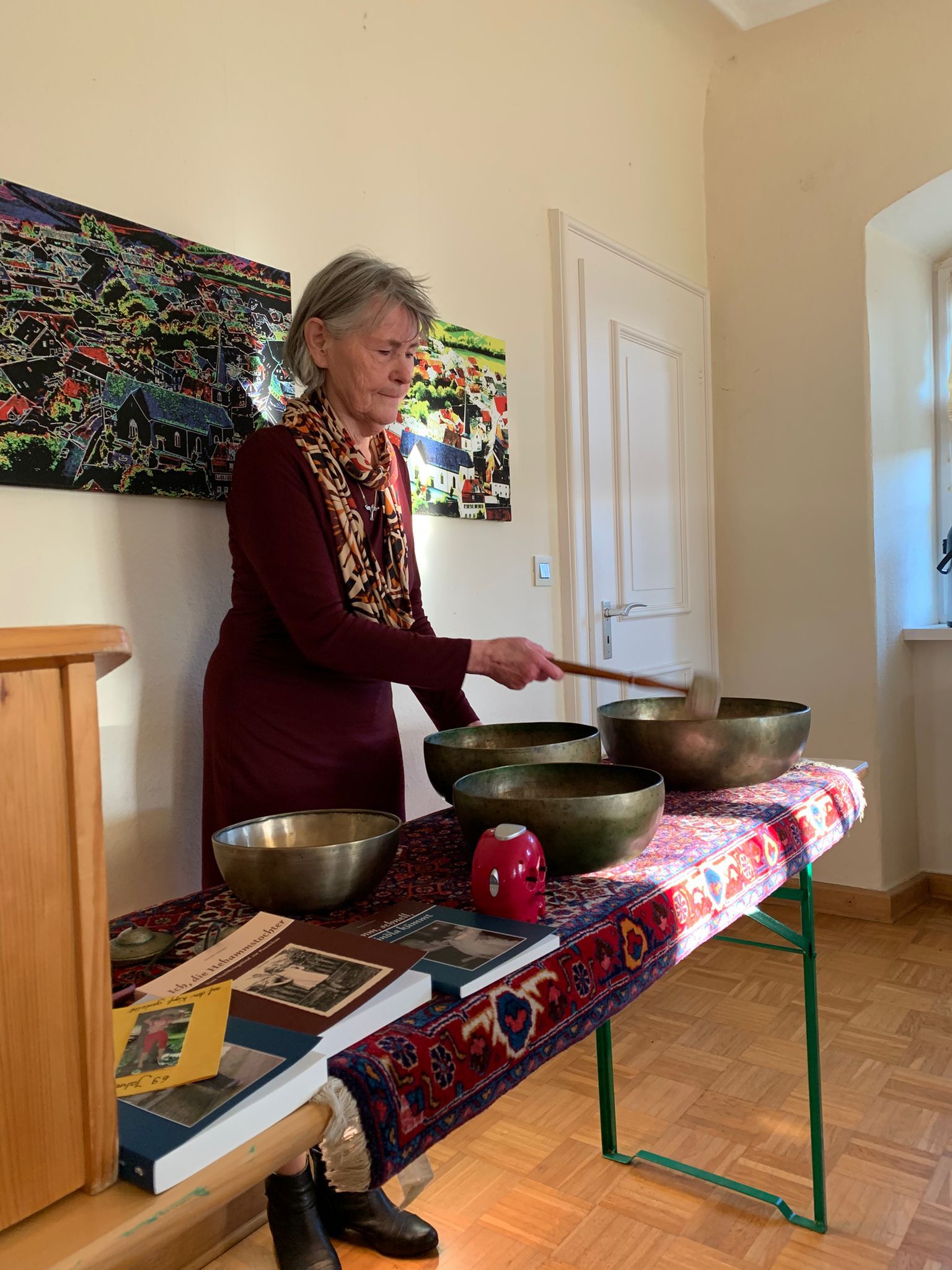 Eine Frau steht vor mehreren Klangschalen und schlägt gerade eine an.