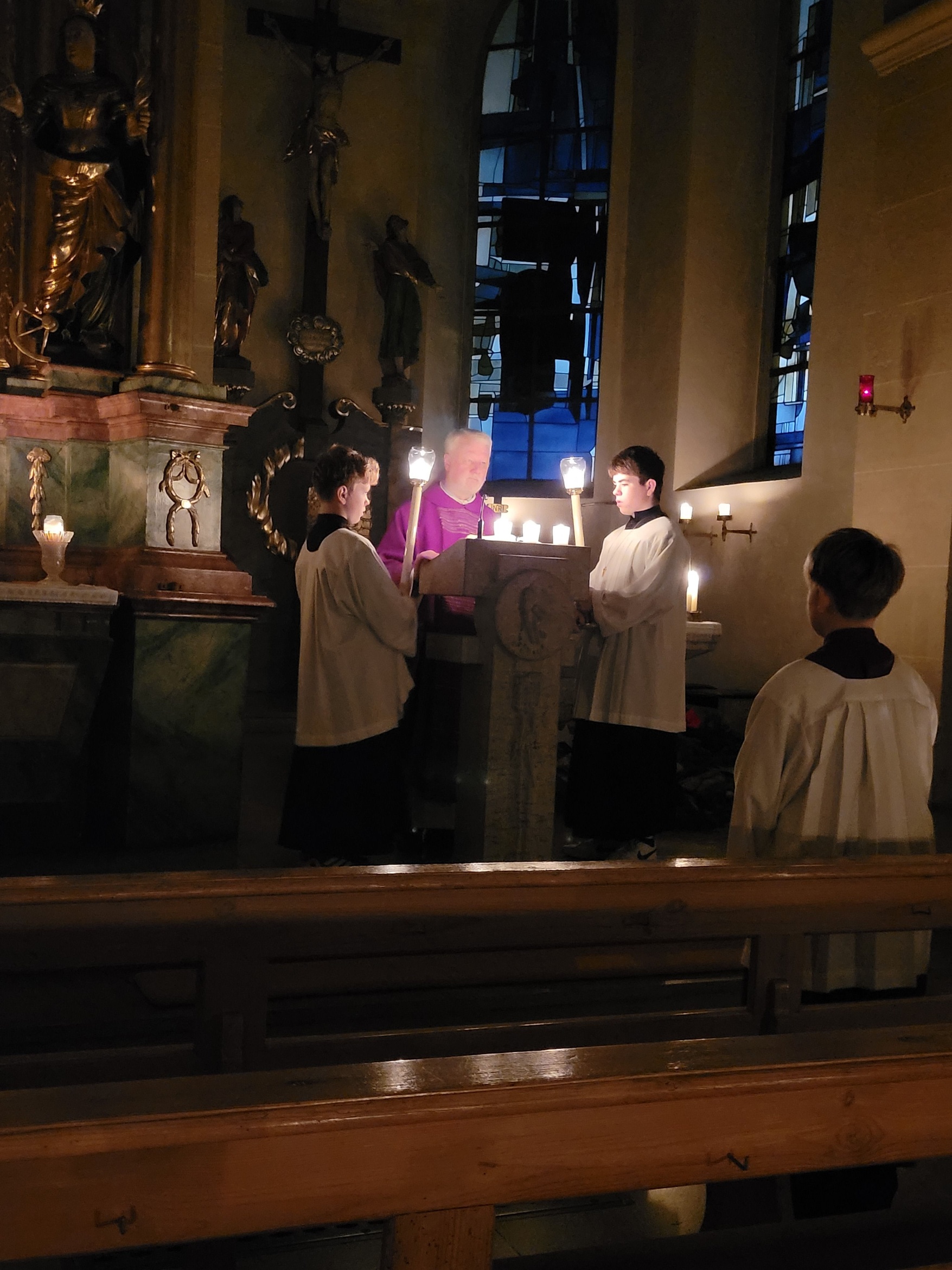 Blick auf den Ambo: Zwei Ministranten stehen rechts und links vom Ambo und halten Leuchter, während der Priester aus der Bibel liest