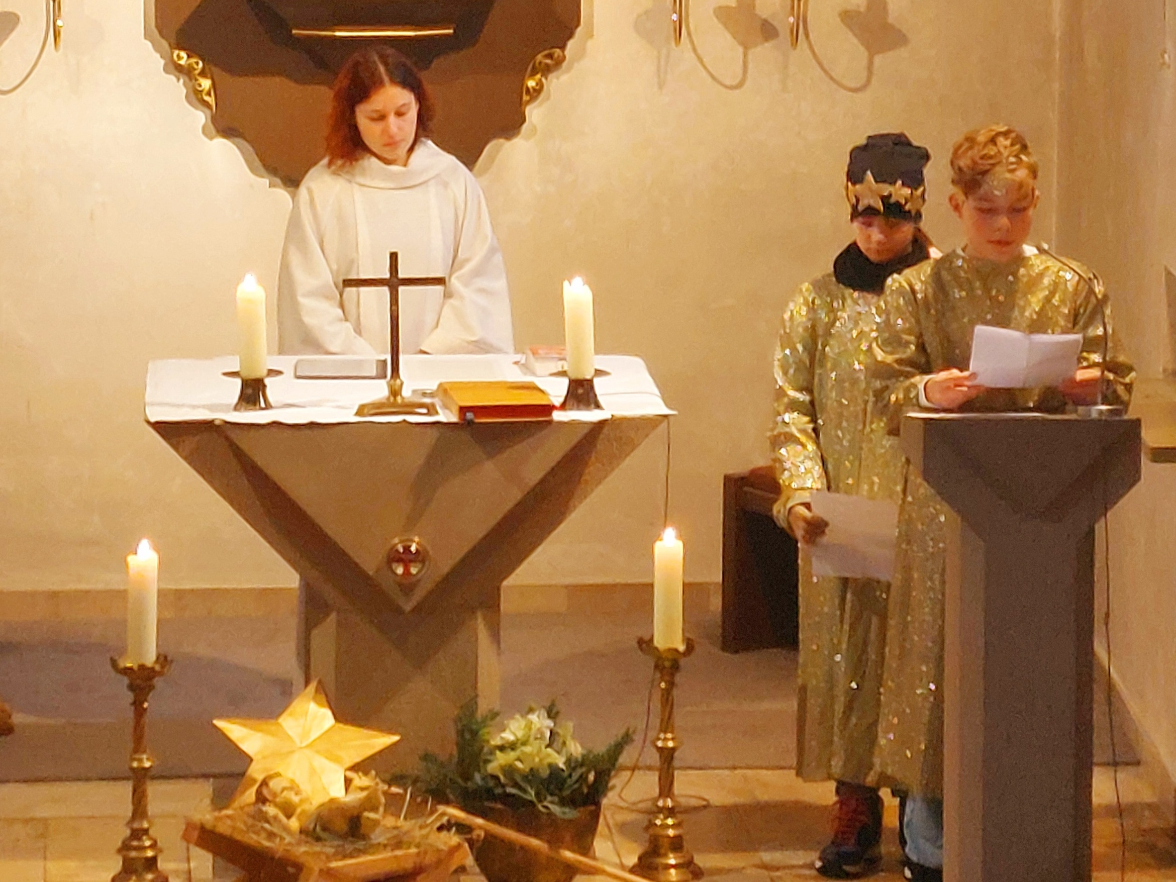 Blick vom Kirchenraum zum Altarraum. Zwei Sternsinger stehen am Ambo und lesen etwas vor.