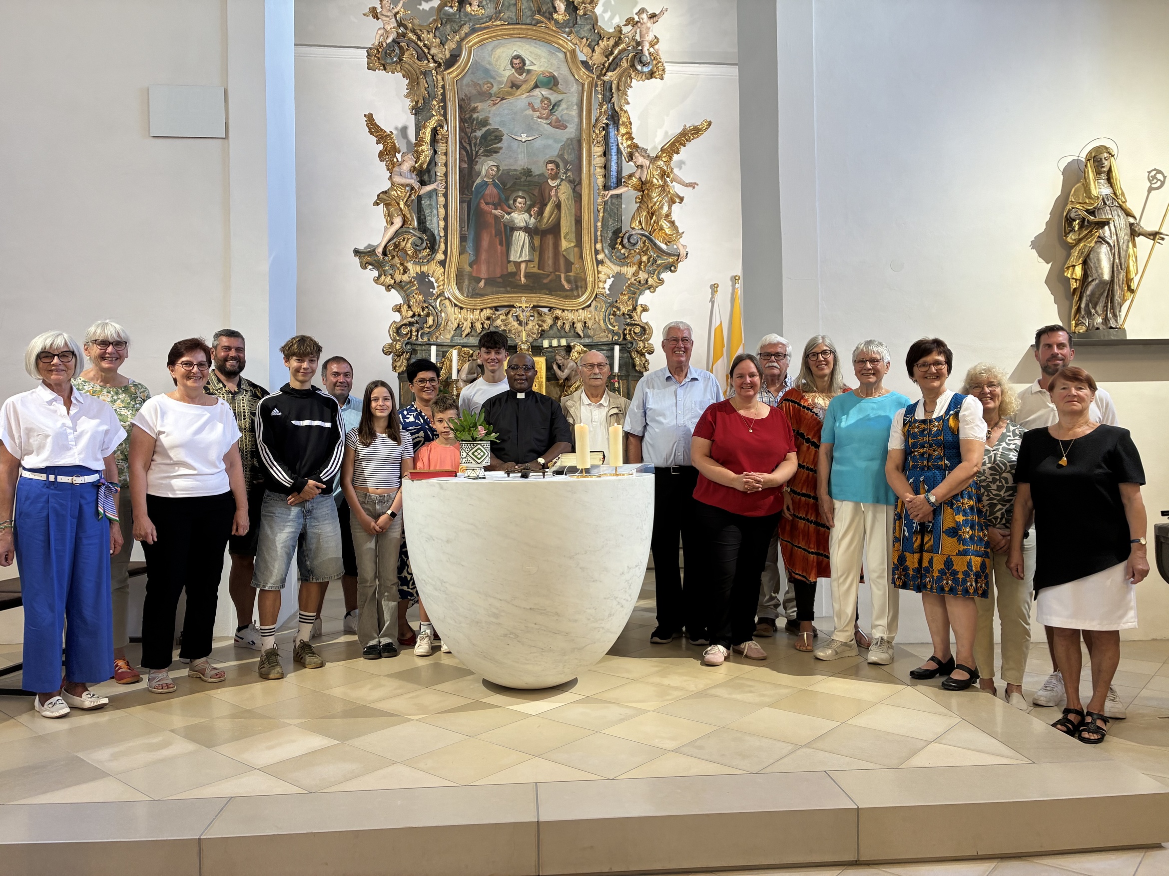 Das Bild zeigt eine Gruppe von Menschen in einer Kirche hinter einem Altar. In der Mitte ist der Priester, der verabschiedet wird.