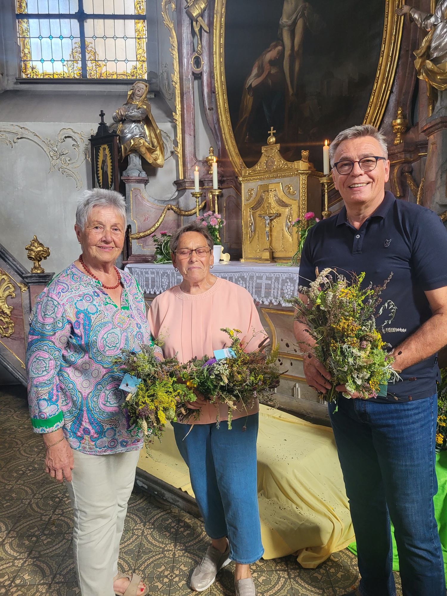 Drei Personen stehen in einer Kirche und halten Kräuterbüschel in der Hand.
