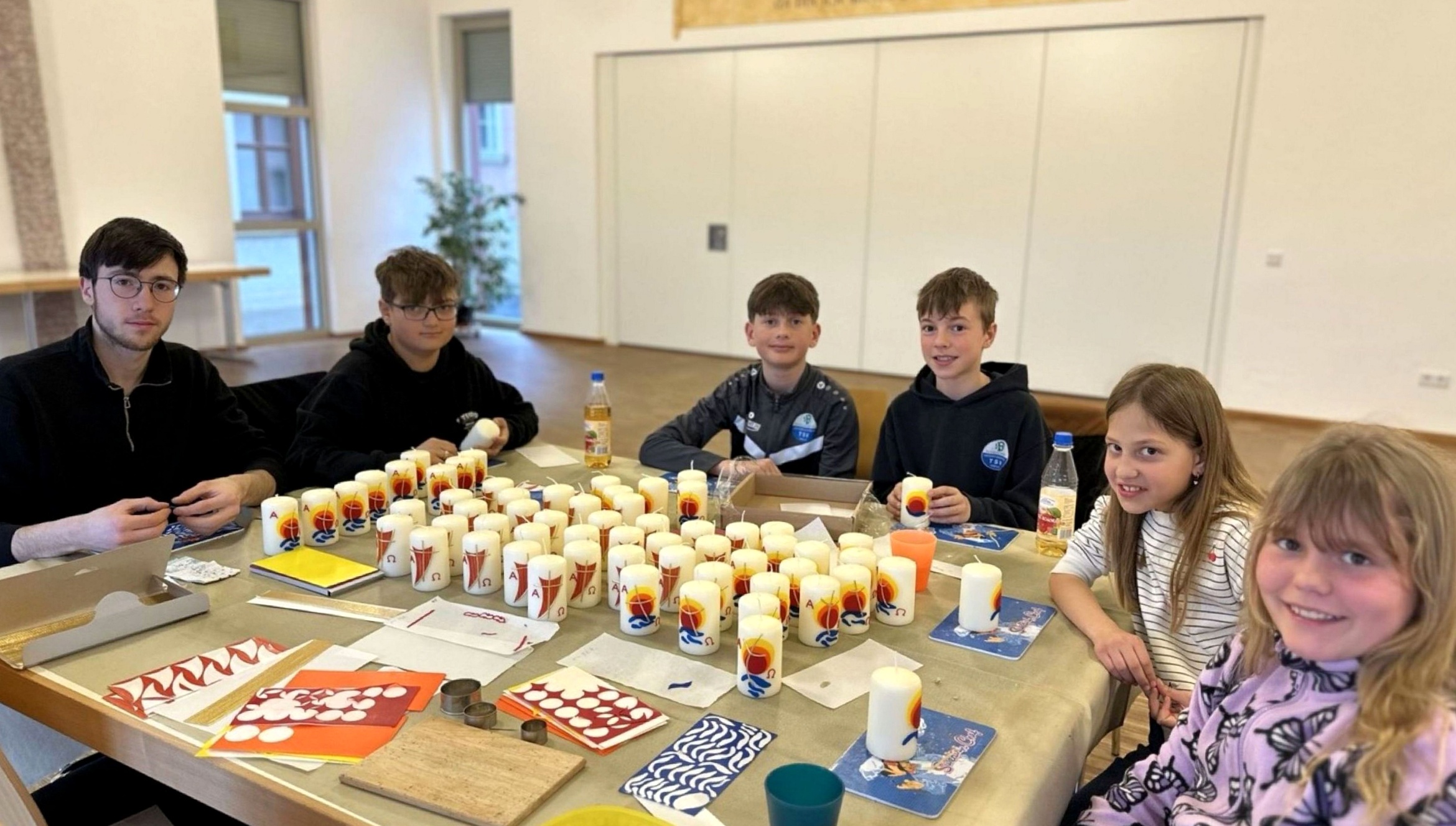 Eine Gruppe an Kindern und Jugendlichen sitzen um einen Tisch. Darauf stehen verzierte Kerzen.