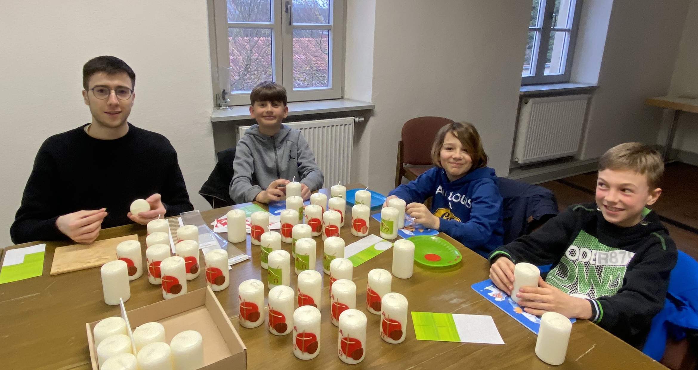 Vier Kinder sitzen um einen Tisch und verzieren Kerzen. Auf dem Tisch stehen viele Kerzen.
