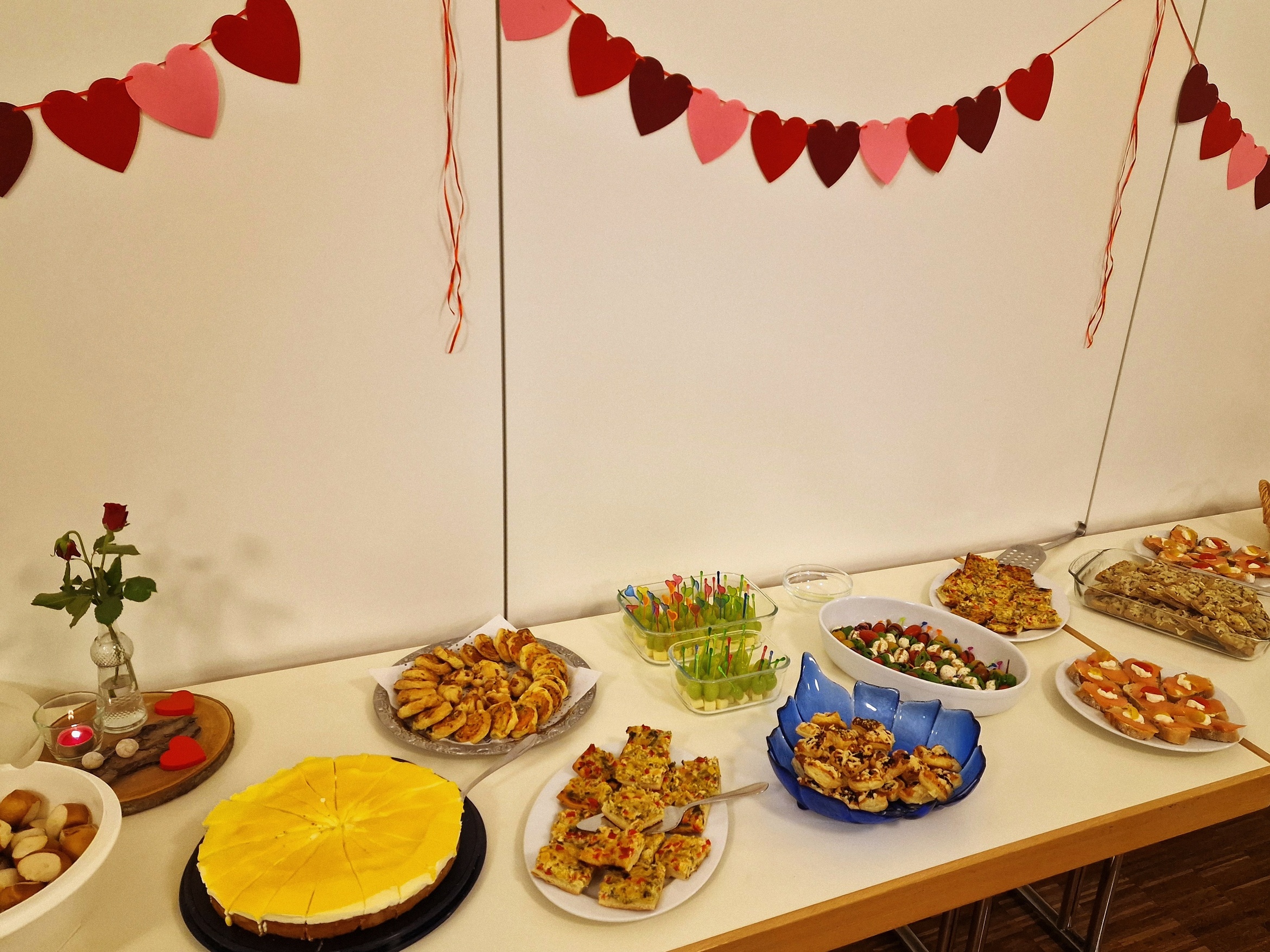 Ein gedeckter Tisch mit allerlei Essensangeboten. An der Wand hängt eine Girlande mit Herzchen.
