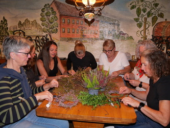 An einem Tisch sitzen Frauen und binden Heidekränzchen.