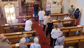 Ein Bild von den Eporen aus ins Kirchenschiff, wo sich im Mittelgang mehrere Menschen zum Empfang der Kommunion anstellen.