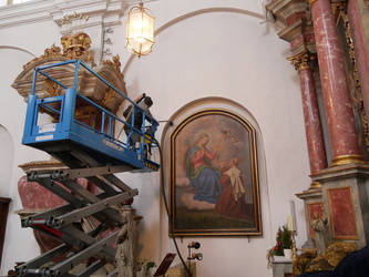 Zwei Männer in einer Hebebühne. Man sieht, wie ein großes Bild gereinigt wird.