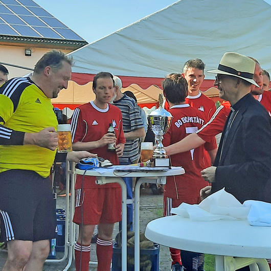 Um einen weißen Stehtisch gruppieren sich Fußballer im Trikot und der Würzburger Bischof Franz Jung.