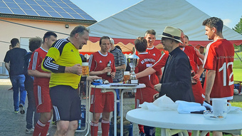 Um einen weißen Stehtisch gruppieren sich Fußballer im Trikot und der Würzburger Bischof Franz Jung.
