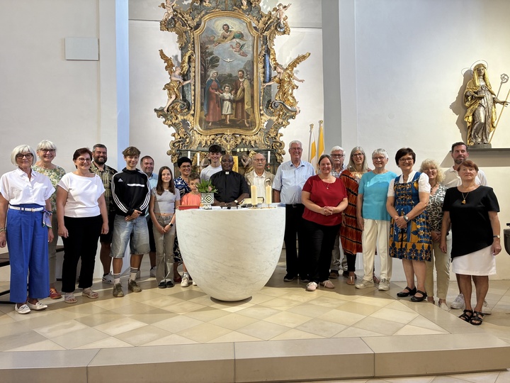 Das Bild zeigt eine Gruppe von Menschen in einer Kirche hinter einem Altar. In der Mitte ist der Priester, der verabschiedet wird.