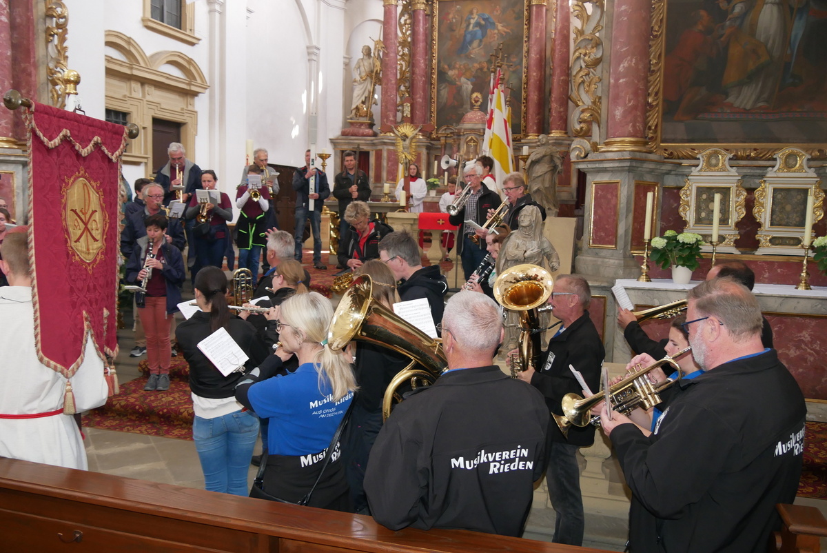 In der Wallfahrtskirche an den Stufen zum Altarraum spielen mehrere Musikanten ein Blasinstrument. Eine Fahne ist auch zu sehen.