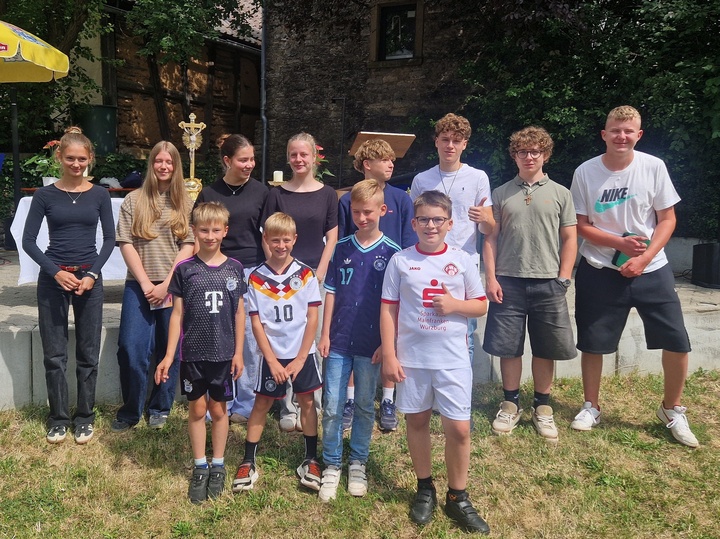 Das Bild zeigt eine Gruppe junger Menschen in einem Garten mit grünem Rasen. Die Stimmung ist fröhlich.