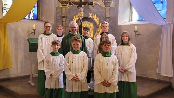 Das ist ein Gruppenbild, auf dem alle zur Kamera schauen. Pfarrer Rügamer steht in der Kirche zwischen neun Ministraten.