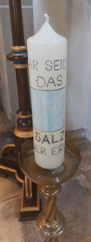 Eine weiße Kerze mit dem Text "Ihr seid das Salz der Erde" in Gold geschrieben.