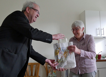 Auf dem Bild sind zwei Personen. Pfarrer Rügamer übergibt Auguste Weber eine Geschenktüte. Es steht danke darauf.