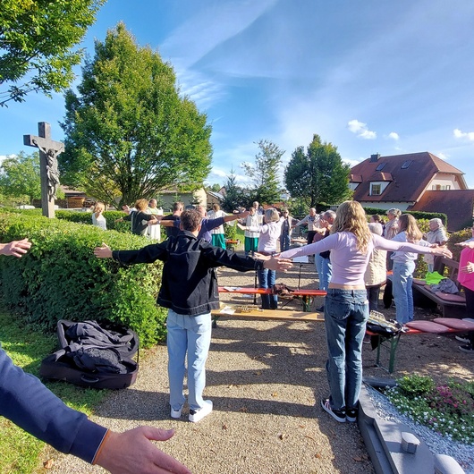 Auf dem Friedhof in Püssensheim stehen Menschen und machen eine weite Bewegung mit den Händen.