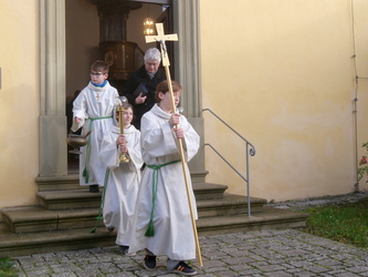 Die Ministranten mit dem Kreuz voran kommen aus der Kirchen-Seitentüre.