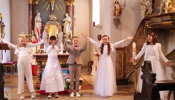 Die fünf Kommunionkinder stehen auf der Stufe zum Altarraum und machen ausladende Gesten zum Lied.