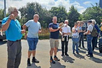 Eine kleine Männergruppe steht bei ihren Oldtimer-Traktoren. Sie lachen.