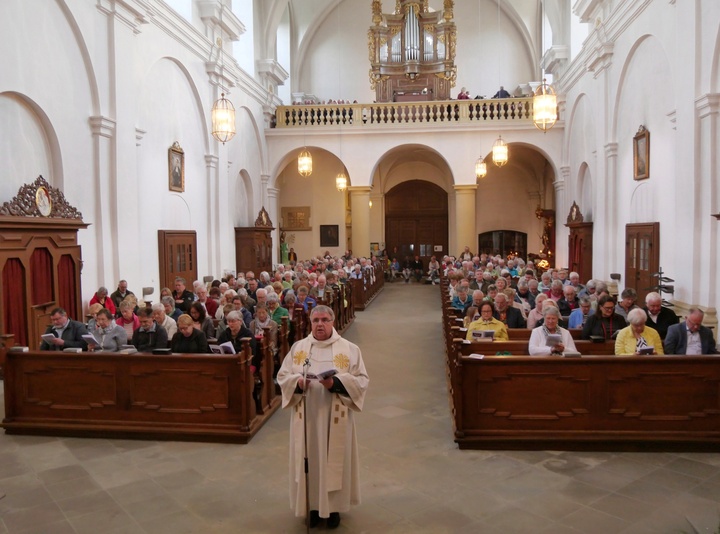 Blick vom Altarraum hinunter in das Kirchenschiff. In der Mitte steht der Domkapitular. Die Bänke sind voll besetzt.