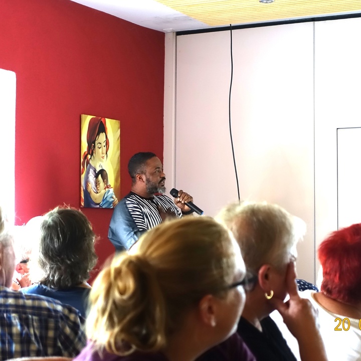Das Foto ist vom Sitzplatz in der Versammlung aufgenommen. Man sieht den Referenten im Hintergrund. Alle blicken zur Präsentation an der Wand.