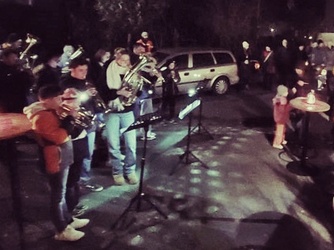 Es ist ein winterliches und dunkles Foto. Eine Musikkapelle spielt auf einer Dorfstraße.