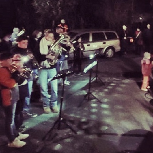 Es ist ein winterliches und dunkles Foto. Eine Musikkapelle spielt auf einer Dorfstraße.