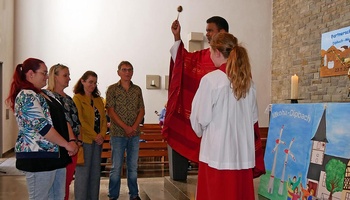 Ein Priester segnet vier Personen, die vor ihm stehen, mit Weihwasser.