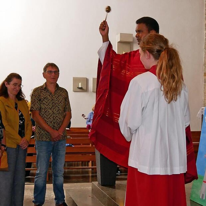 Ein Priester segnet vier Personen, die vor ihm stehen, mit Weihwasser.