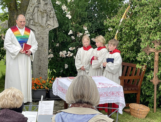 Der Wortgottesdienstleiter steht links von einem Bildstock und spricht. Recht vom Bildstock sieht man drei Ministranten.