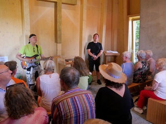 Blick von hinten in der Kapelle zum Kreuz. Vorne stehen Pfarrer Witzel und Sabine Triebel. Es wird gesungen.