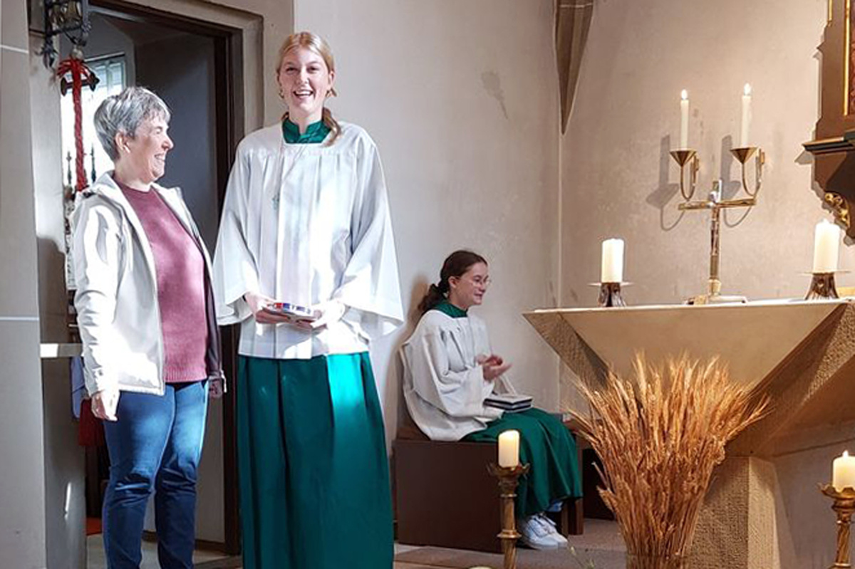 Zwei Frauen stehen in einer Kirche nebeneinander. Sie lächeln freundlich.