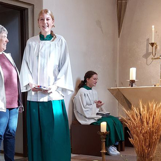 Zwei Frauen stehen in einer Kirche nebeneinander. Sie lächeln freundlich.