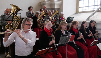 Auf der Empore sitzen Musizierende in Bänken und spielen ihr Instrument.