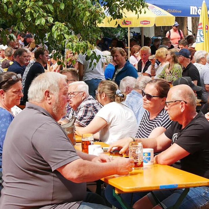 Viele Menschen sitzen an Bierbänken und unterhalten sich.