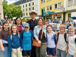 Das Bild zeigt eine Gruppe, die in die Kamera lächelt. Es sind Kinder und Erwachsene zu sehen. Hinten in der Mitte steht ein Bischof.